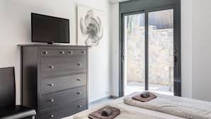 Een slaapkamer met een bed, een televisie op een dressoir, een groot raam en een stenen muur buiten.