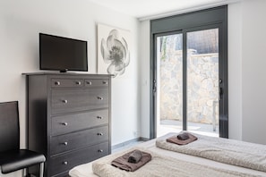 Ein Schlafzimmer mit einem Bett, einem Fernseher auf einer Kommode, einem großen Fenster und einer Steinwand draußen.