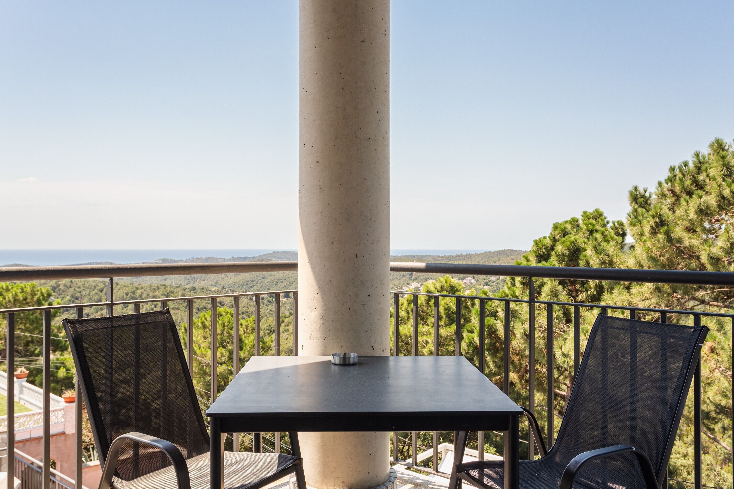 A balcony with a table and chairs, overlooking a mountainous landscape.