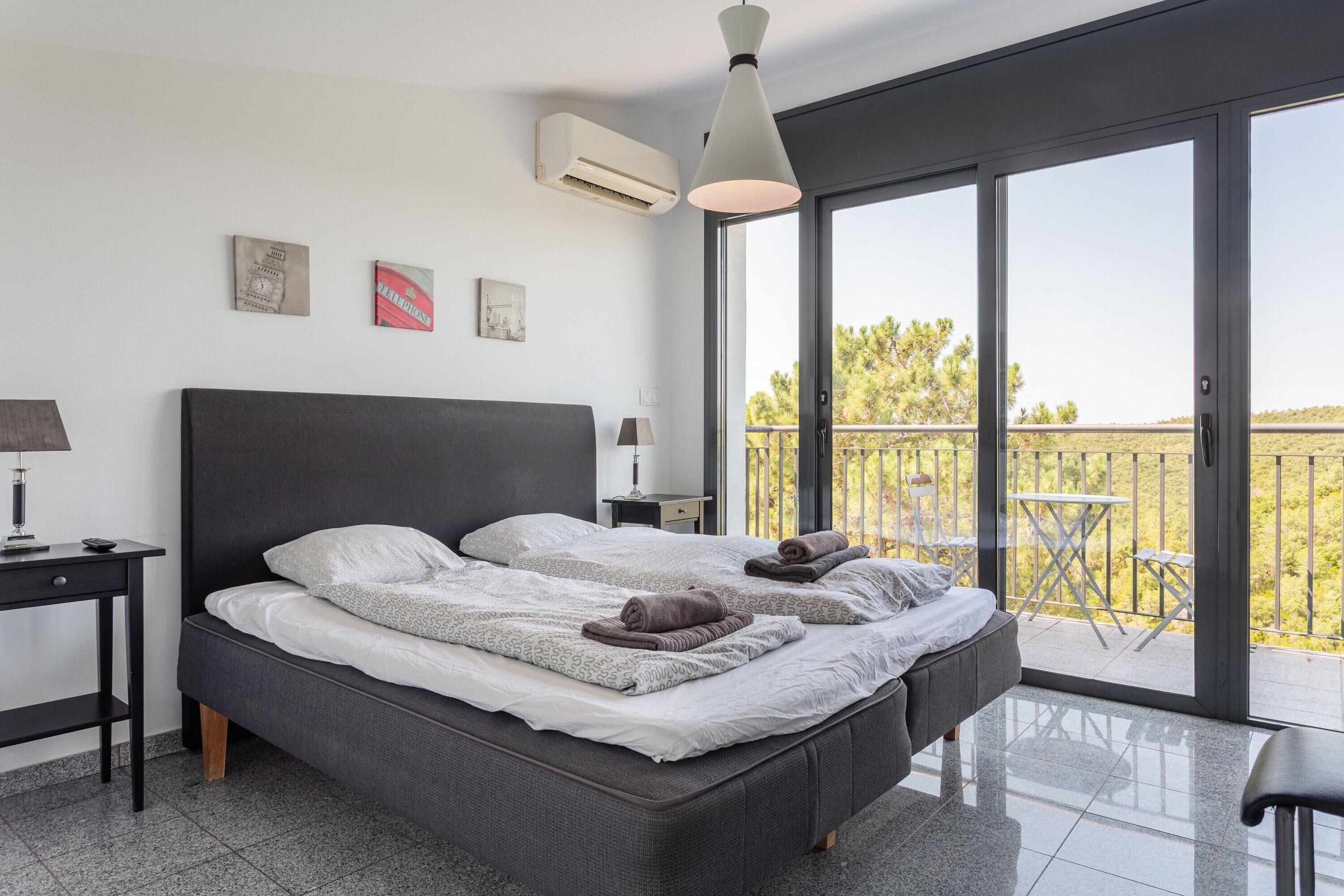A modern bedroom with a large bed, a desk, a chair, and a balcony with a table and chairs.
