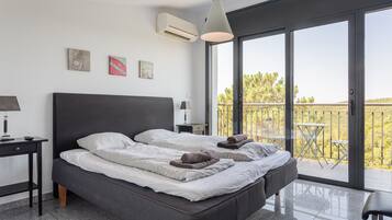 A modern bedroom with a large bed, a desk, a chair, and a balcony with a table and chairs.
