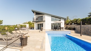 Een modern huis met een zwembad, terras en een balkon.