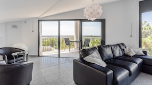 Een moderne woonkamer met een zwarte leren bank, een glazen salontafel en een balkon met uitzicht.