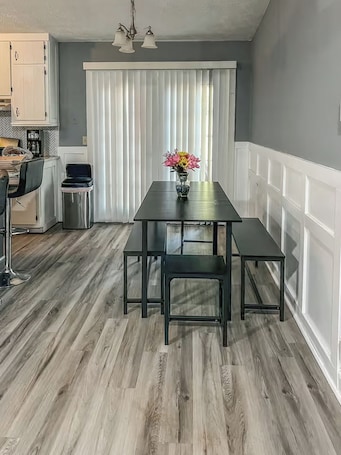 A dining area with a table and benches, a kitchen in the background, and a window with blinds.. Sweet Spot - Entire Home