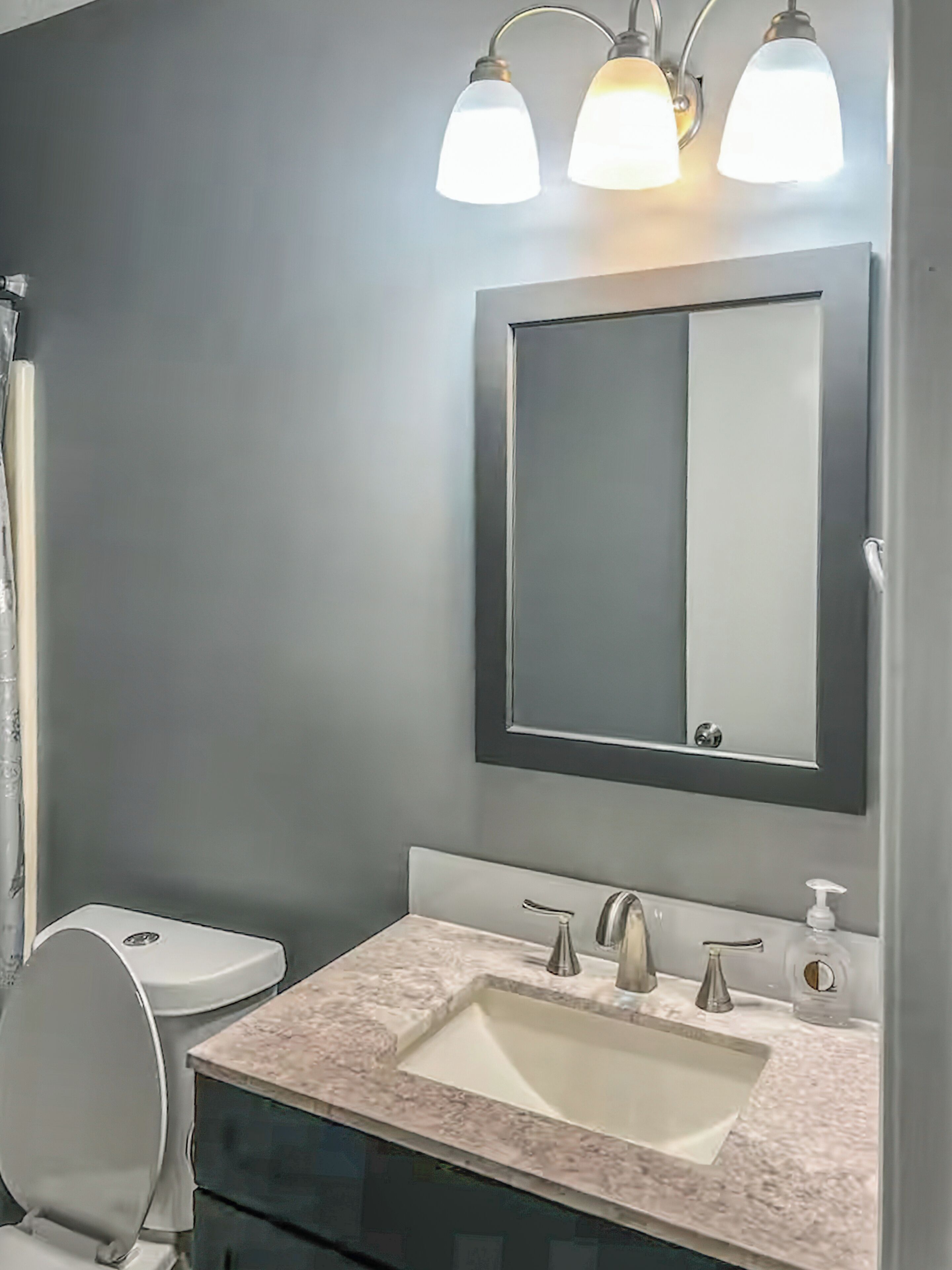 A bathroom with a toilet, sink, mirror, and three wall-mounted lights.