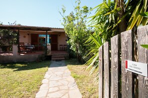 A stone pathway leading to a house with a patio area. A wooden fence with a sign is visible. - Casa del Vento by Wonderful Italy (Olbia)