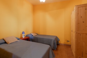 Una habitación con dos camas, una mesita de noche, una lámpara y un armario.