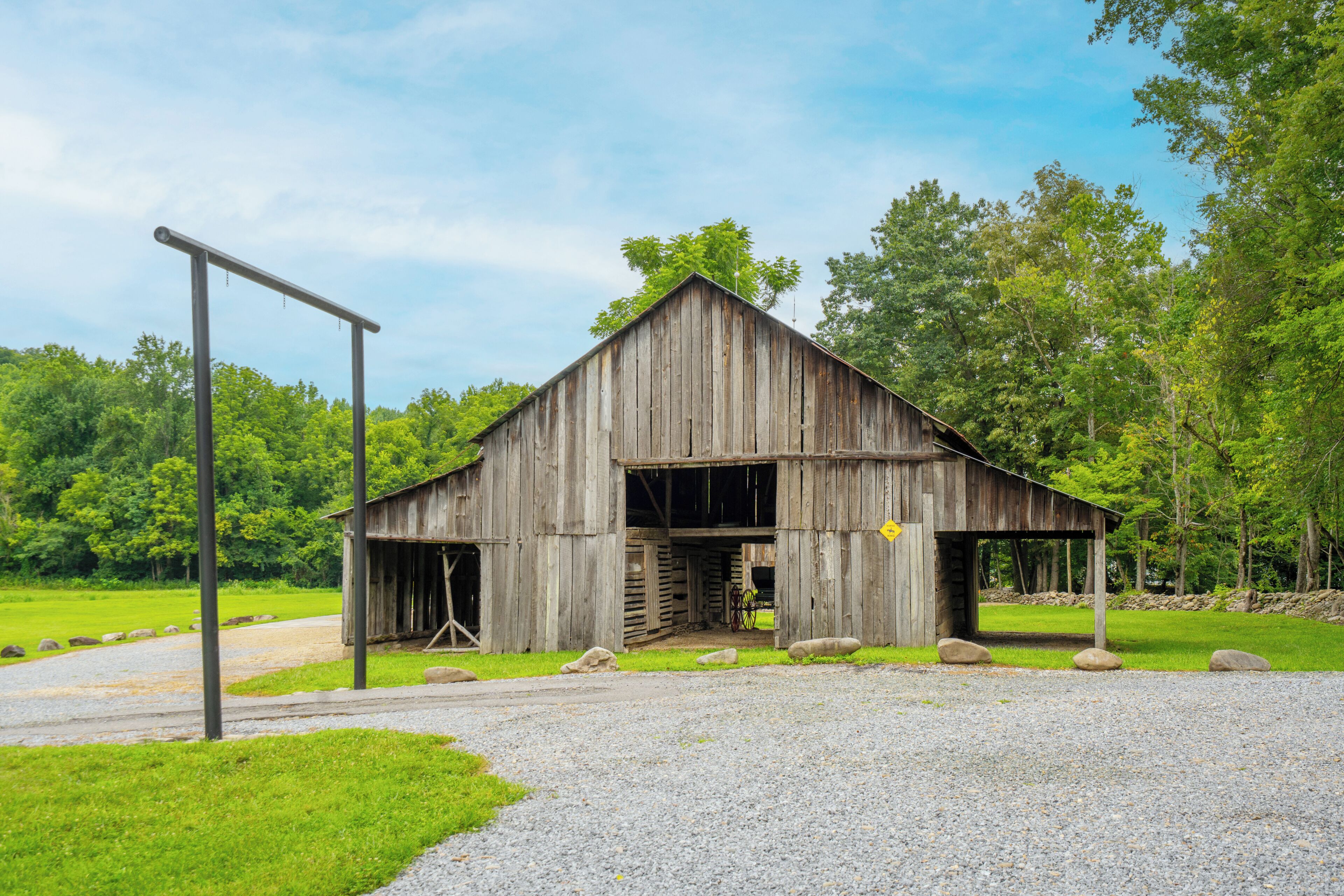 A rustic wooden barn with a gravel driveway and a metal gate.