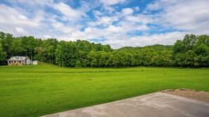 A large, open grassy field with a house and dense trees in the background.