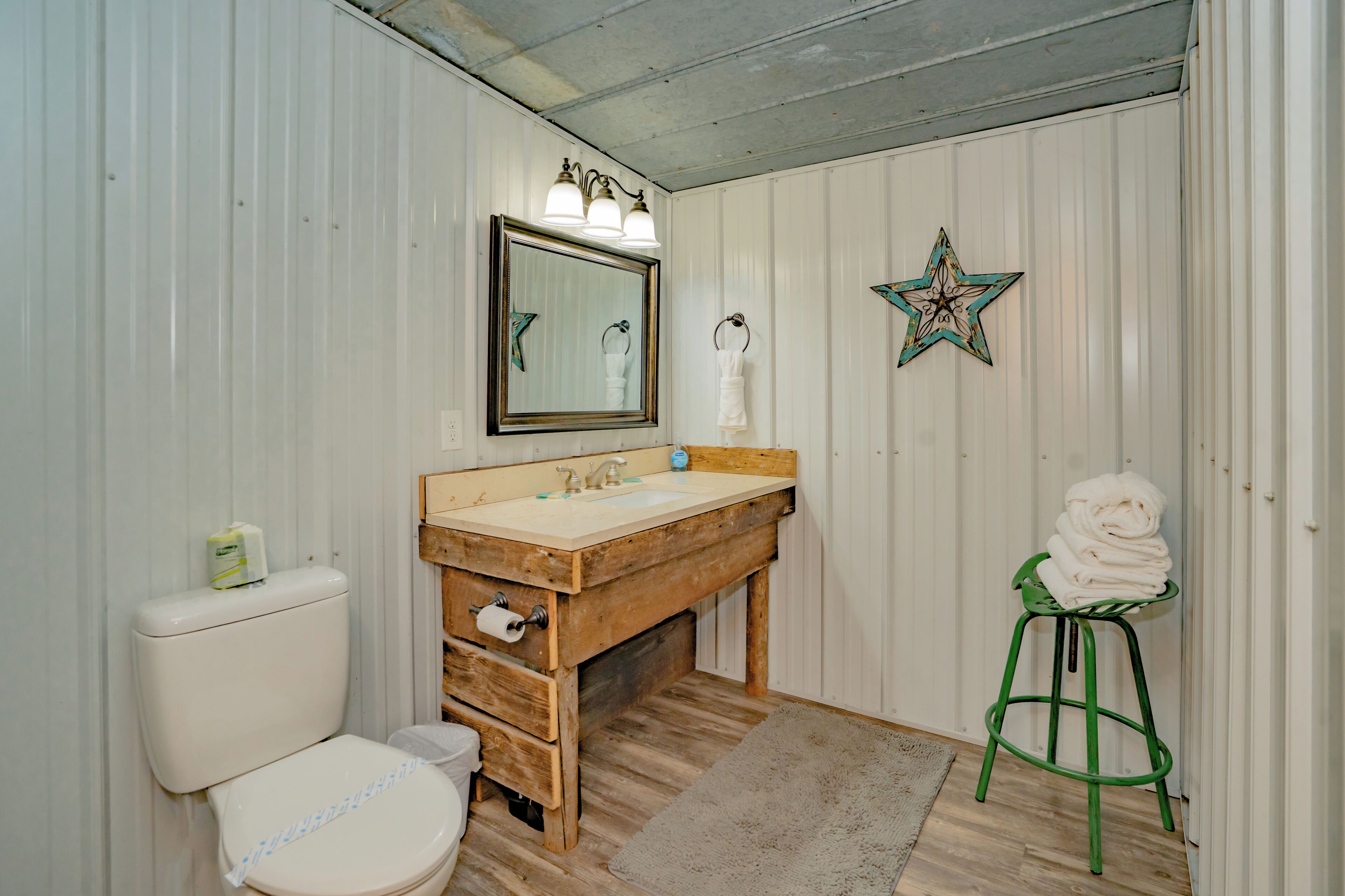 Un baño con tocador de madera, inodoro, espejo con luces y decoración de estrella en la pared.