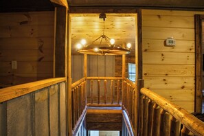 A wooden interior with a central staircase, a hanging light fixture, and a thermostat on the wall.