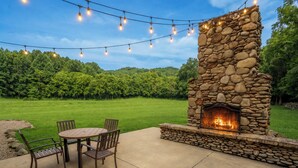 An outdoor patio with a stone fireplace, a round table, and chairs.