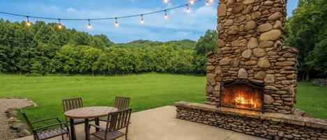 An outdoor patio with a stone fireplace, a round table, and chairs.