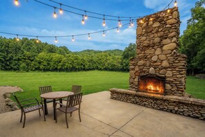 An outdoor patio with a stone fireplace, a round table, and chairs. - TBarnLoft@FF: Honeymoon, Outdoor Fireplace, Wifi, Water View, Large Yard (Cosby)