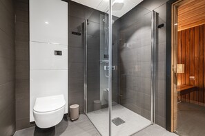 Ein modernes Badezimmer mit einer gläsernen Duschkabine, einer weißen Toilette und einer hölzernen Sitzbank.