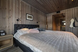 Un dormitori amb un disseny de panells de paret de fusta, un capçal de llit amb guarnició, un llit amb roba de llit estampada, làmpades de nit i un quadre encimbellat a la tauleta de nit.