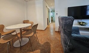 Una habitación con una mesa de comedor y sillas, un sofá, un televisor y una cocina al fondo.