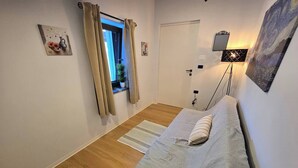 Une chambre à coucher avec un lit, une fenêtre avec des rideaux, une lampe de chevet et un miroir fixé au mur.