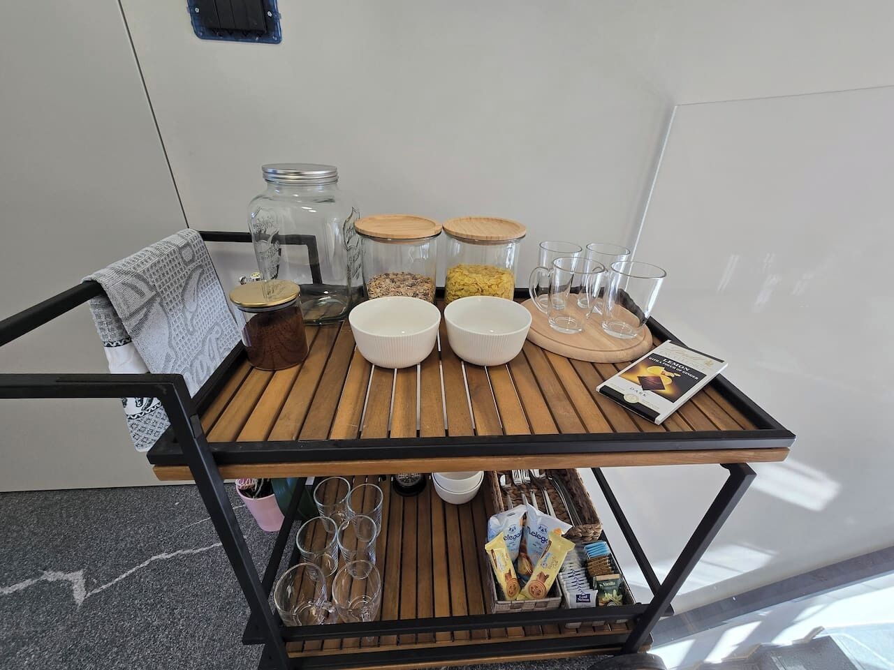A wooden cart with jars, bowls, glasses, and a magazine.