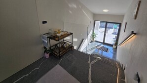 Un couloir avec un chariot en métal, une plante en pot et une vue sur l’extérieur.