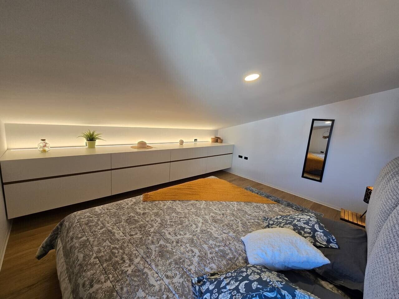 Une chambre à coucher comprenant un lit, une table de chevet, un miroir et un banc intégré.