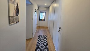 Un couloir étroit au plancher de bois, un tapis à motifs, une fenêtre donnant sur un paysage et une porte sur la droite.