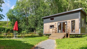 A cabin with a wooden exterior, a gravel path leading to it, and a red umbrella in the foreground. - Le Petit Haras De Valmont Chalet with Private Terrace, Garden, and Air Conditioning (Valmont)