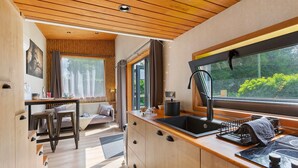 A compact kitchen with wooden cabinets, a sink, and a window overlooking greenery. - Le Petit Haras De Valmont Chalet with Private Terrace, Garden, and Air Conditioning (Valmont)