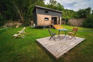 Une petite cabane dotée d’une terrasse, de sièges d’extérieur et d’un mur de pierres en arrière-plan.