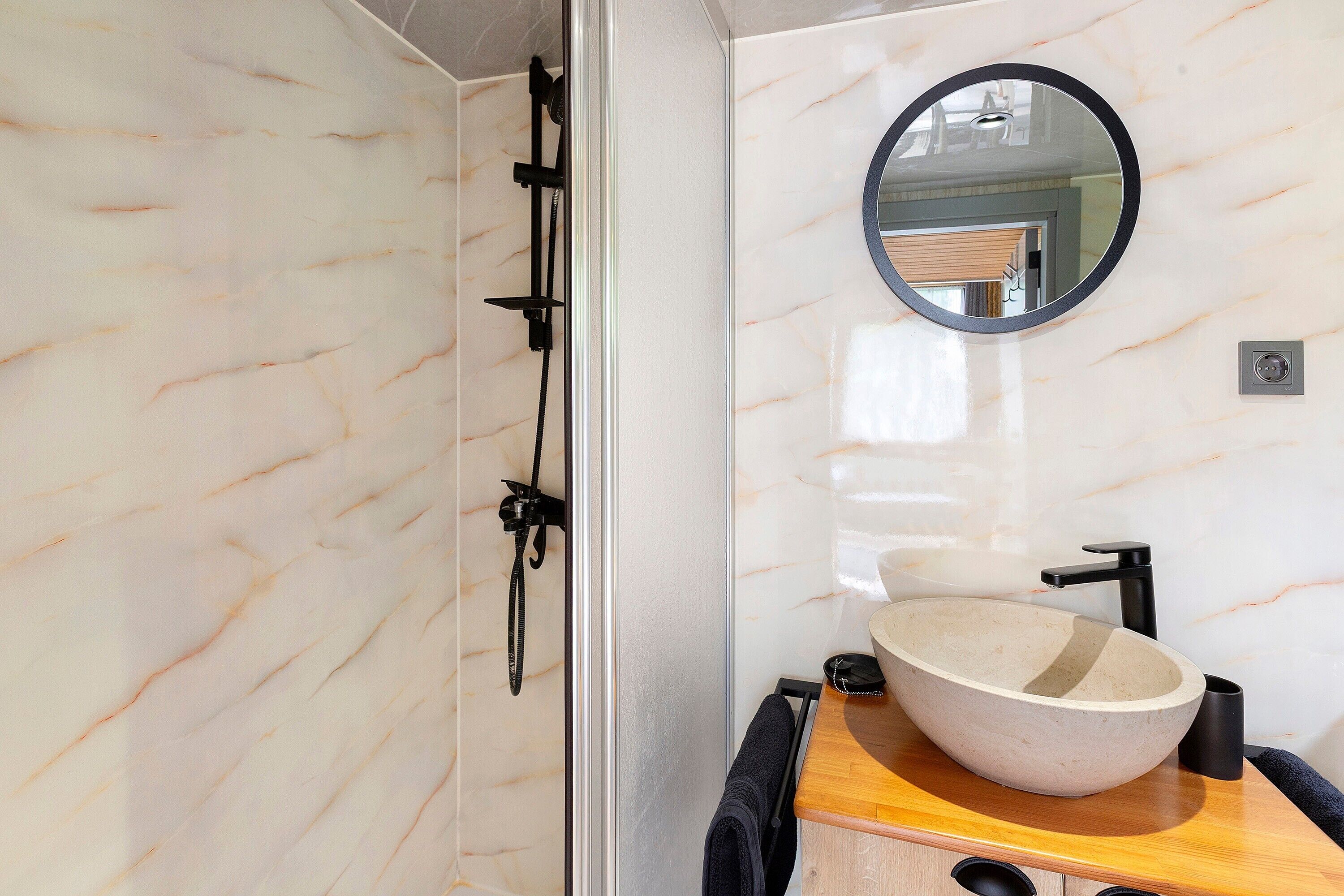 Een badkamer met een marmeren wand, een houten wastafelmeubel, een ronde spiegel en een moderne wastafel.