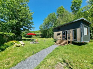 Une petite cabane avec une véranda, un parasol rouge et un chemin de gravier menant à l’entrée.