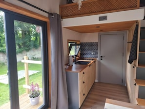 Eine kleine Küche mit Spüle, Holzschränken, einem Fenster und Blick ins Grüne.
