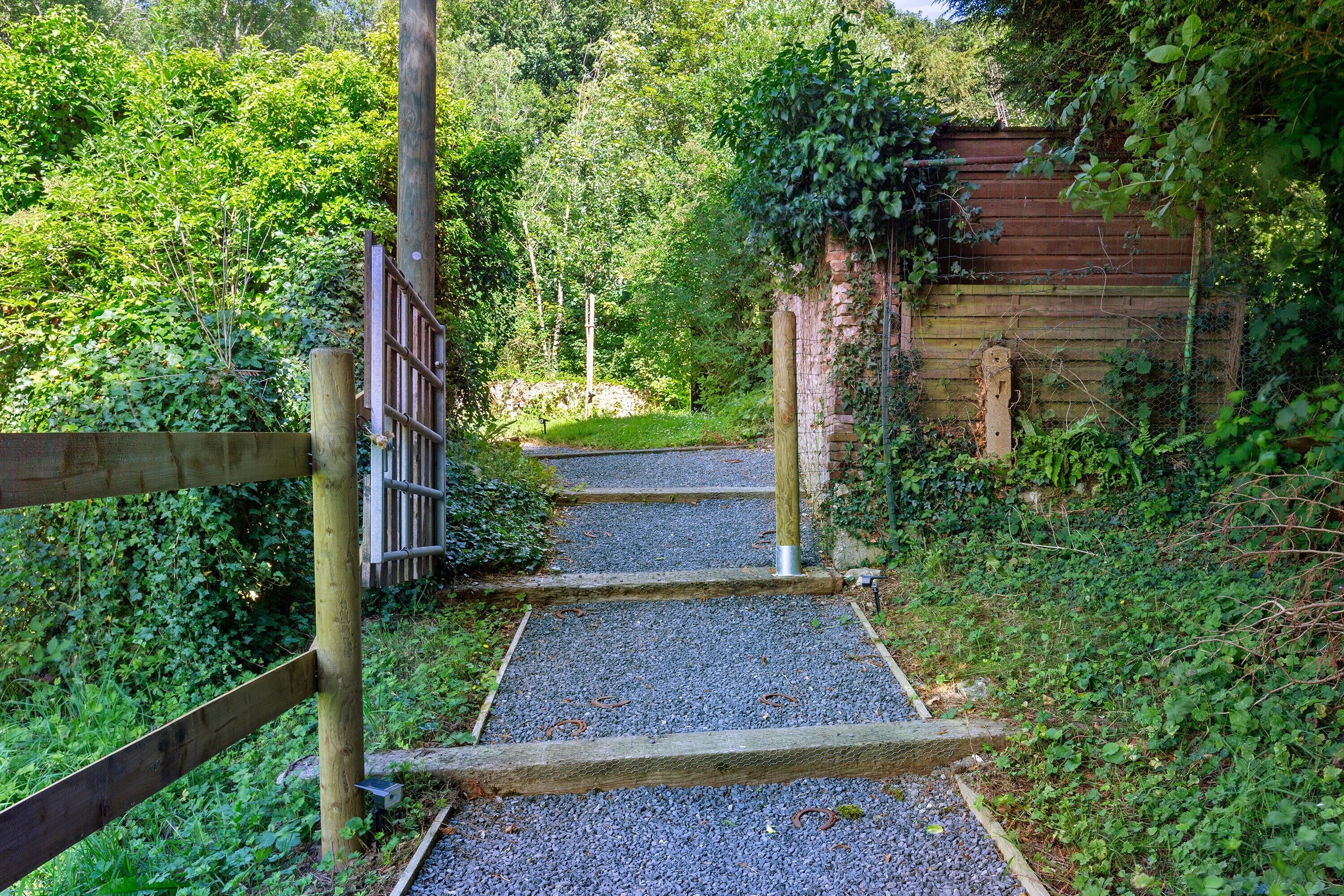 Un chemin de gravier mène à une structure en bois, elle-même entourée de verdure.