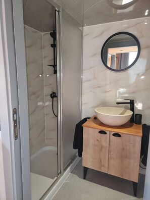 A modern bathroom with a glass shower enclosure, a wooden vanity with a large basin, and a round mirror.