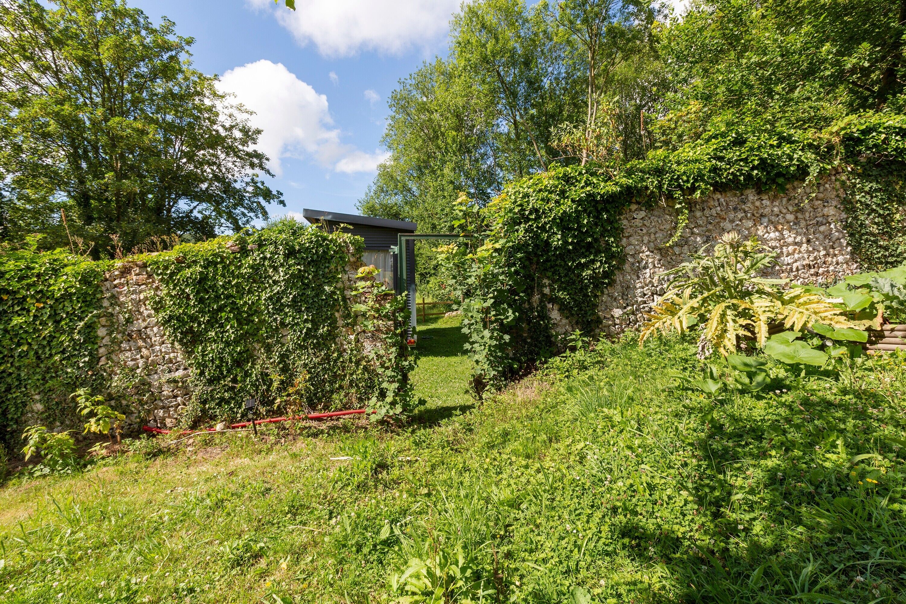 Un mur de pierre, une petite construction et une végétation luxuriante.