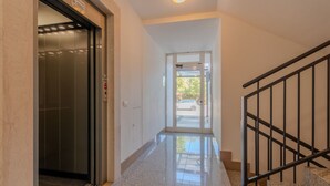 Ein Korridor mit einer Glastür zu einem Aufzug, einer Treppe mit Metallgeländer und einer Tür, die nach draußen führt.
