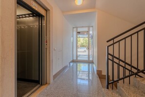 Ein Korridor mit einer Glastür zu einem Aufzug, einer Treppe mit Metallgeländer und einer Tür, die nach draußen führt.