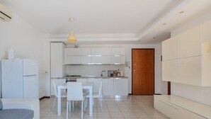 Eine moderne Küche mit weißen Schränken, einem Esstisch mit Stühlen, einem Kühlschrank und einer Holztür.