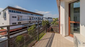 Ein Balkon mit Metallgeländer, der auf ein Wohngebäude mit zahlreichen Fenstern und Balkonen blickt.