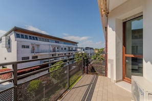 Ein Balkon mit Metallgeländer, der auf ein Wohngebäude mit zahlreichen Fenstern und Balkonen blickt.