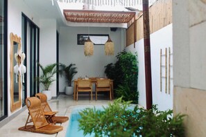 Un área de comedor exterior moderna con piscina, mobiliario de mimbre y plantas en macetas.