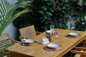 A wooden dining table set with plates, glasses, and a centerpiece, surrounded by wicker chairs and greenery. - Strategically located near Canggu, Seminyak, and various public facilities. (Badung)