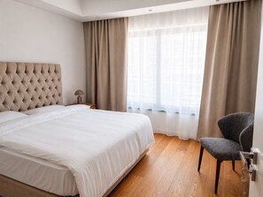 A hotel room with a large bed, a chair, a nightstand, and a window with curtains. - Apartment 1 (Lemesos)