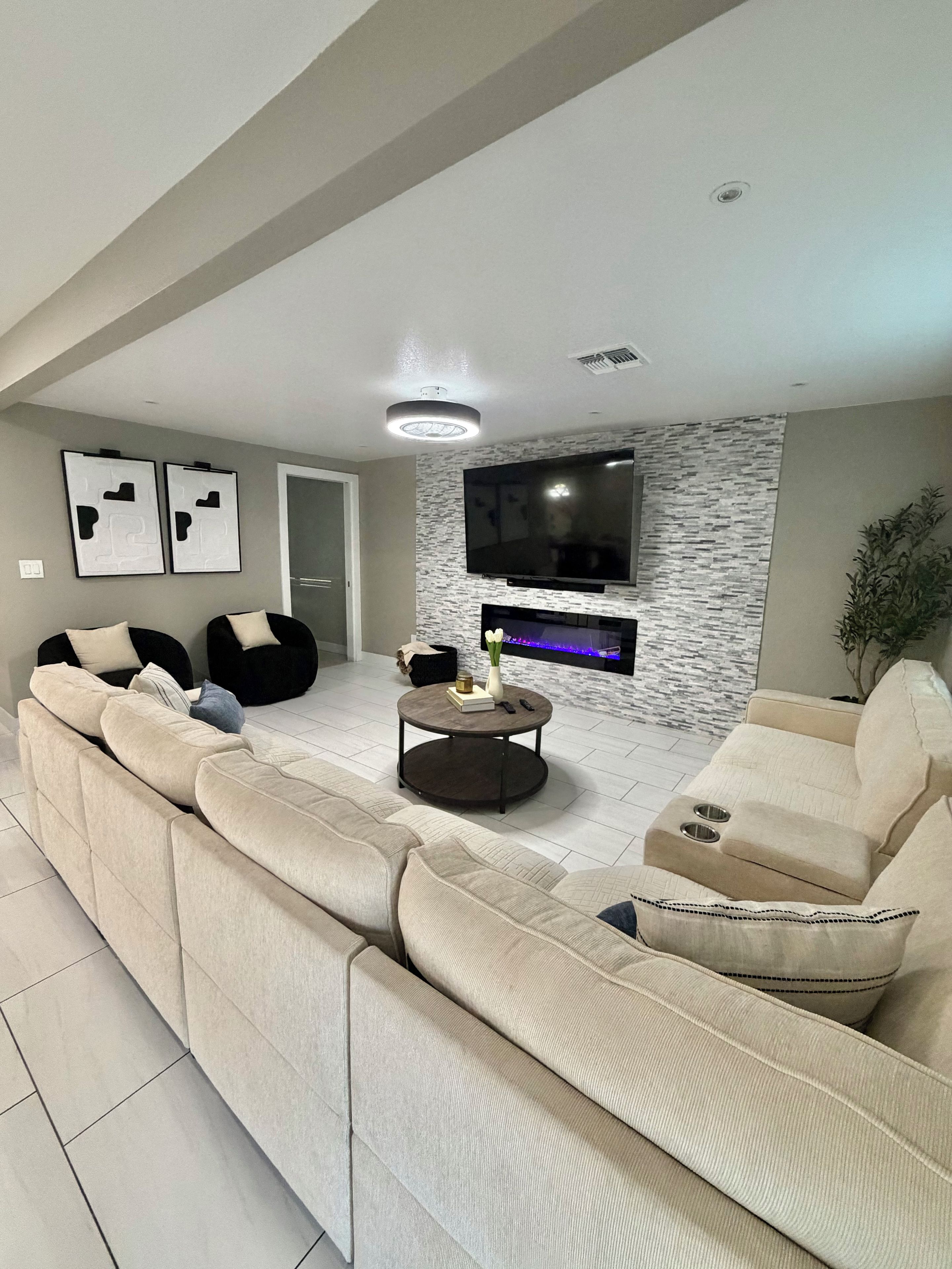 A modern living room with a sectional sofa, a flat-screen TV mounted on a textured wall, and a round coffee table with decorative items.