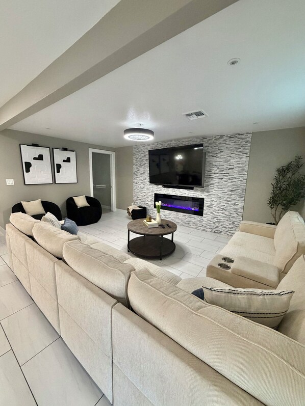 A modern living room with a sectional sofa, a flat-screen TV mounted on a textured wall, and a round coffee table with decorative items. - House in Las Vegas, NV  (North Las Vegas)