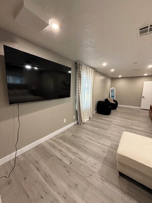 Una habitación con televisión de pantalla plana en la pared, un sillón de peluche, una cama y una puerta.