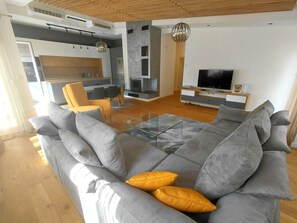 A modern living room with a grey sectional sofa, a glass coffee table, and a TV. - Cozy 2-bedroom apartment in peaceful Skopje with AC (Skopje)