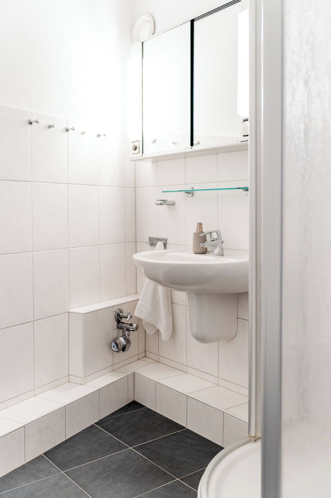 A bathroom with a white sink, a glass shelf, a towel hanging on the wall, and a bathtub.