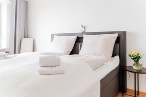 A neatly made bed with white linens and pillows, a bedside table with a vase of flowers, and a chair in a modern hotel room. - Vacation apartment "FjordHavn" on the 8th floor of the Viking Tower (Schleswig)