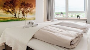 Hotelkamer met een bed, een schilderij van bomen, een raam met uitzicht en een handdoek op het bed.